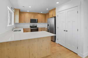 Kitchen with a peninsula, light brown cabinets, appliances with stainless steel finishes, light wood-type flooring, and recessed lighting