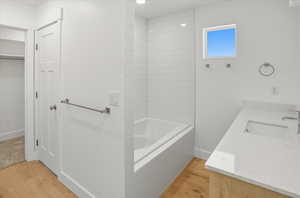 Bathroom featuring light wood-style flooring, vanity, a walk in closet, and tiled shower / bath