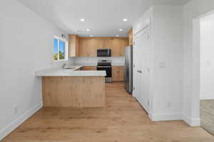 Kitchen with a peninsula, light brown cabinetry, appliances with stainless steel finishes, recessed lighting, and light wood finished floors