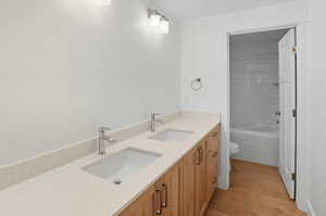 Bathroom with double vanity, light wood-style flooring, and tiled shower / bath