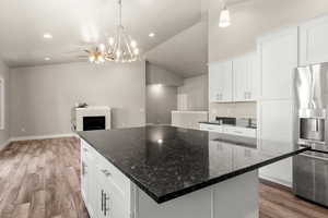 Kitchen with white cabinetry, stainless steel refrigerator with ice dispenser, dark stone counters, light wood finished floors, and vaulted ceiling