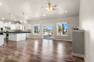 Unfurnished living room featuring healthy amount of natural light, a chandelier, a ceiling fan, dark wood-style floors, and recessed lighting