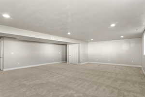 Finished below grade area featuring light colored carpet, a textured ceiling, and recessed lighting