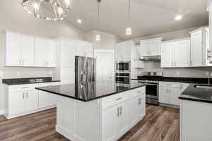 Kitchen featuring stainless steel appliances, dark stone counters, pendant lighting, dark wood finished floors, and vaulted ceiling