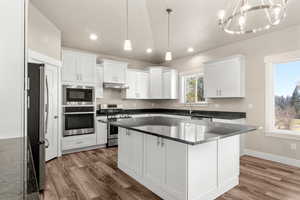 Kitchen with stainless steel appliances, white cabinetry, a kitchen island, decorative light fixtures, and dark stone counters