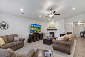 Living area featuring vaulted ceiling, a warm lit fireplace, ceiling fan, recessed lighting, and carpet