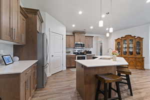 Kitchen featuring brown cabinetry, arched walkways, tasteful backsplash, a center island with sink, and hanging light fixtures
