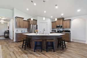 Kitchen featuring tasteful backsplash, arched walkways, a kitchen breakfast bar, decorative light fixtures, and lofted ceiling
