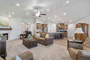 Living room featuring a ceiling fan, arched walkways, light carpet, a fireplace, and recessed lighting