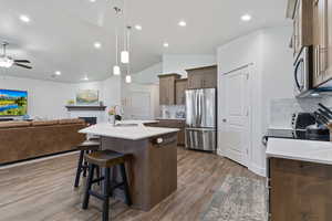 Kitchen with decorative light fixtures, vaulted ceiling, light wood finished floors, a kitchen island with sink, and open floor plan
