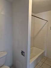 Full bath with light tile patterned floors, a textured ceiling, and shower / bath combination