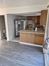 Kitchen with tile counters, a textured ceiling, brown cabinetry, light wood finished floors, and a peninsula