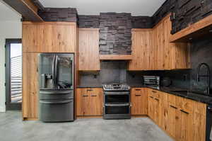 Kitchen featuring stainless steel appliances, decorative backsplash, concrete floors, dark stone counters, and modern cabinets