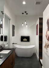 Bathroom featuring double vanity, a freestanding bath, finished concrete flooring, and recessed lighting
