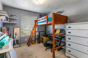 Bedroom featuring a textured ceiling, an office area, and light carpet