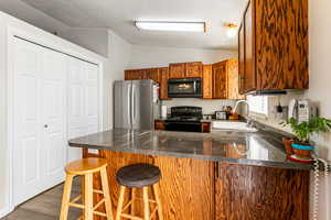 Kitchen featuring a peninsula, brown cabinets, black appliances, lofted ceiling, and a breakfast bar area