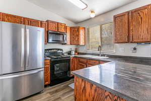 Kitchen featuring black appliances, dark countertops, a textured ceiling, dark wood-type flooring, and brown cabinetry
