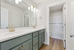 Full bath featuring double vanity, dark wood finished floors, and washtub / shower combination