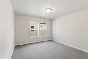 Carpeted spare room featuring a textured ceiling and baseboards