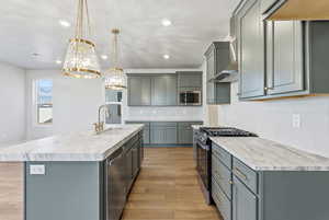 Kitchen featuring appliances with stainless steel finishes, light wood finished floors, an island with sink, decorative backsplash, and gray cabinets