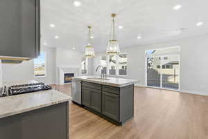 Kitchen with open floor plan, a glass covered fireplace, light wood-style floors, gray cabinets, and hanging light fixtures