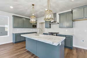 Kitchen with wall chimney exhaust hood, pendant lighting, decorative backsplash, a kitchen island with sink, and dark wood-style floors