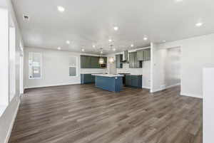 Kitchen with open floor plan, tasteful backsplash, a center island with sink, dark wood finished floors, and decorative light fixtures