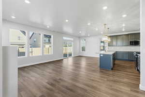 Kitchen with a kitchen island with sink, open floor plan, tasteful backsplash, hanging light fixtures, and dark wood finished floors