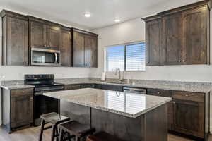 Kitchen with appliances with stainless steel finishes, light stone countertops, dark brown cabinets, a breakfast bar area, and a center island