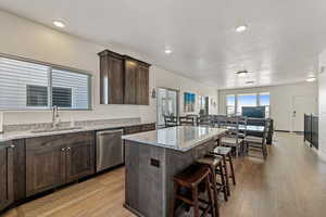 Kitchen featuring dark brown cabinetry, open floor plan, light wood-style floors, light stone countertops, and a center island