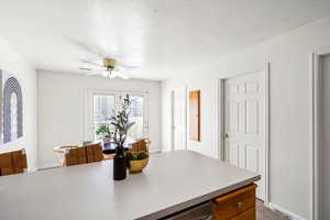 Kitchen with a textured ceiling, ceiling fan, light countertops, and brown cabinets