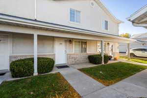 Doorway to property featuring brick siding, stucco siding, covered porch, and a yard