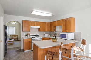 Kitchen with white appliances, a breakfast bar, brown cabinetry, a peninsula, and light countertops