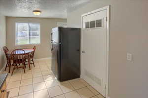 Kitchen featuring freestanding refrigerator, light tile patterned floors, and a textured ceiling