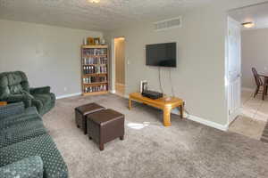 Living room featuring a textured ceiling, light colored carpet, and light tile patterned flooring