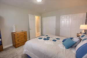 Bedroom featuring two closets, a textured ceiling, and light carpet