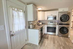 Kitchen with appliances with stainless steel finishes, light wood-style floors, white cabinetry, a textured ceiling, and stacked washer / drying machine