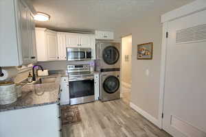 Kitchen with appliances with stainless steel finishes, white cabinetry, a textured ceiling, dark stone counters, and light wood-style flooring