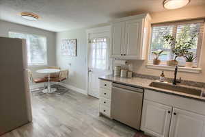 Kitchen featuring freestanding refrigerator, a textured ceiling, white cabinets, stainless steel dishwasher, and dark stone countertops