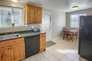 Kitchen with black appliances, light tile patterned floors, dark countertops, and a textured ceiling