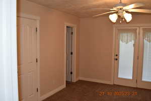Unfurnished room featuring ceiling fan, dark carpet, and a textured ceiling