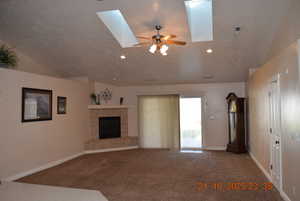 Unfurnished living room with carpet floors, a tile fireplace, lofted ceiling, a ceiling fan, and a skylight