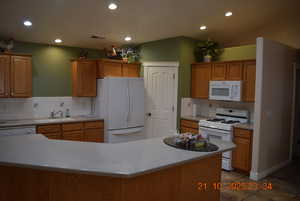Kitchen featuring white appliances, recessed lighting, tasteful backsplash, brown cabinets, and dark tile patterned flooring