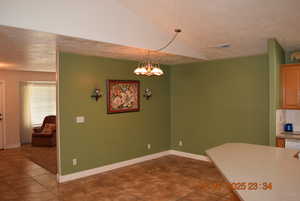 Dining area featuring a textured ceiling, a chandelier, dark tile patterned flooring, and lofted ceiling