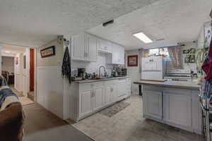 Kitchen featuring light countertops, white cabinetry, white appliances, a peninsula, and a textured ceiling