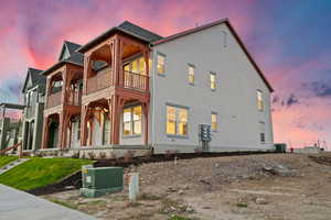 Back of property at dusk featuring a porch, stucco siding, and a shingled roof