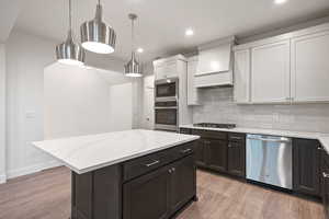 Kitchen with tasteful backsplash, stainless steel appliances, hanging light fixtures, light wood-style flooring, and light stone counters