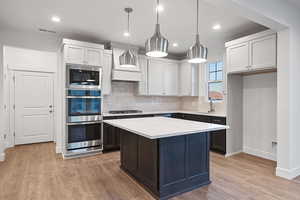 Kitchen with decorative backsplash, decorative light fixtures, light wood finished floors, white cabinets, and appliances with stainless steel finishes