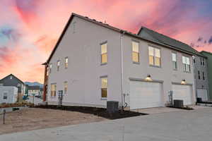 Property exterior at dusk featuring an attached garage, concrete driveway, and stucco siding