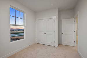 Unfurnished bedroom with light carpet, a water view, and a closet